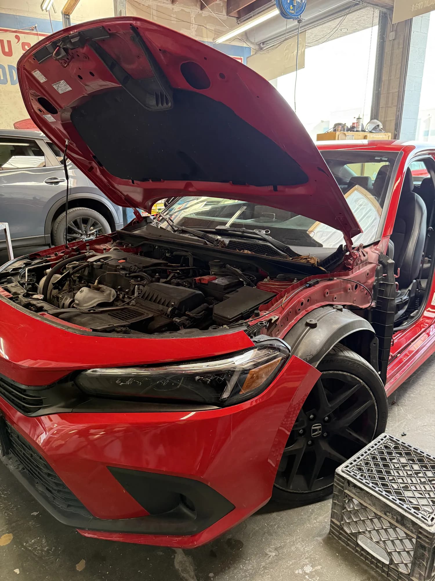 Honda Civic with front-end damage and the hood raised in the workshop