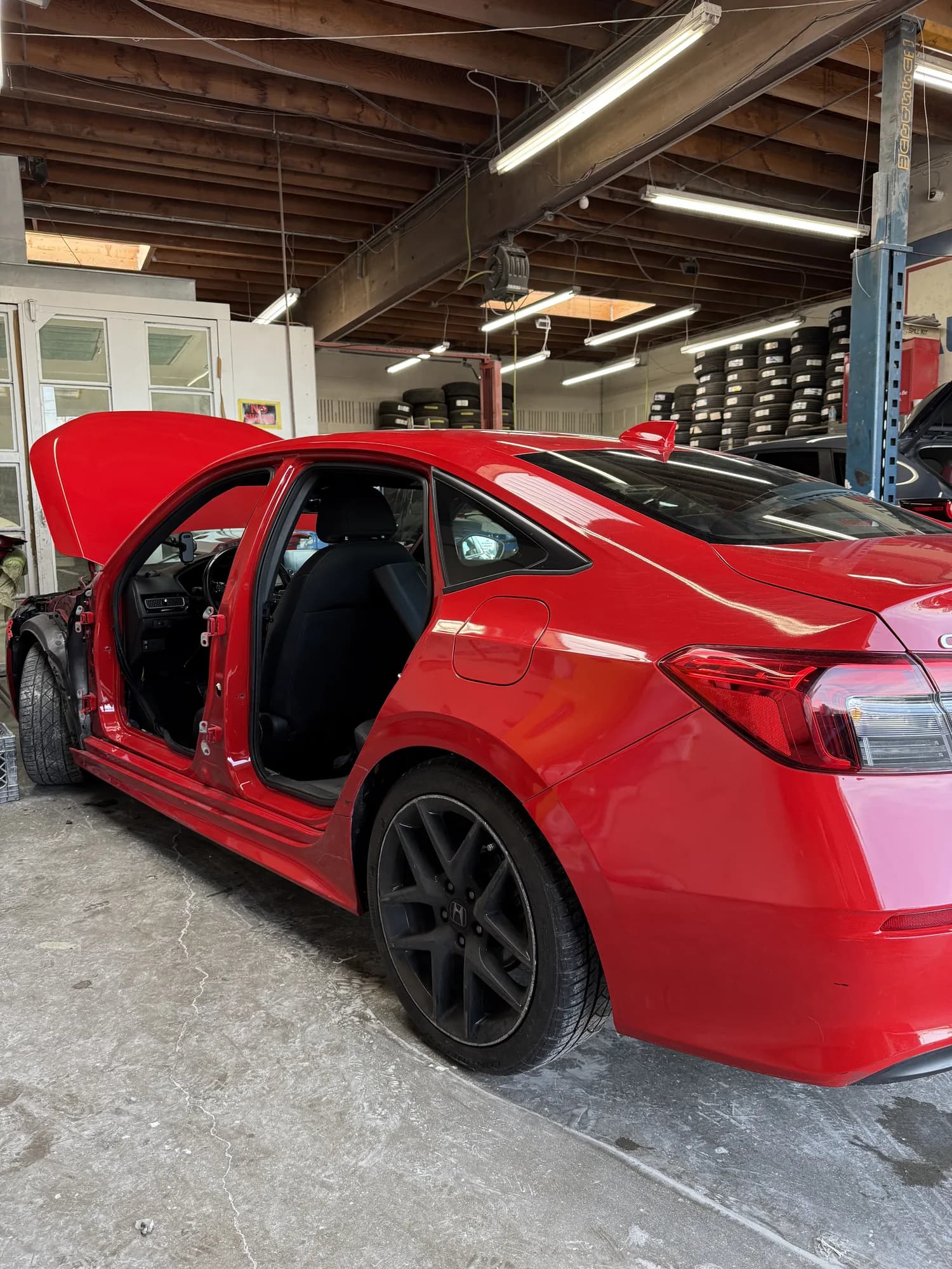 Red Honda Civic in the workshop with doors open during repair