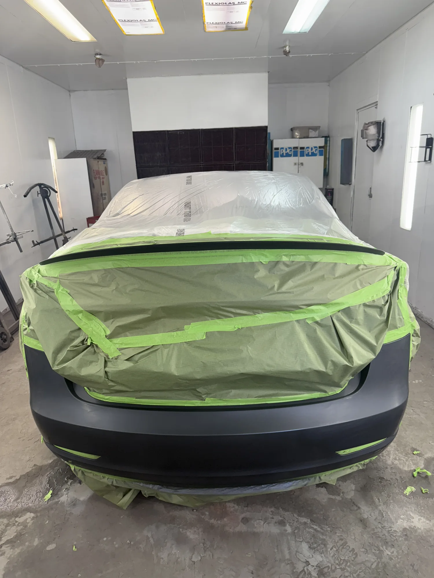 Rear of a vehicle masked in green tape and plastic before painting